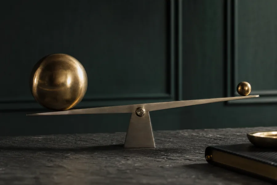 A steel balance holding two brass spheres of unequal size, representing leverage