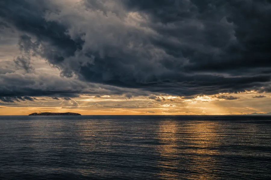 Storm clouds gathering over a calm dark sea at dusk